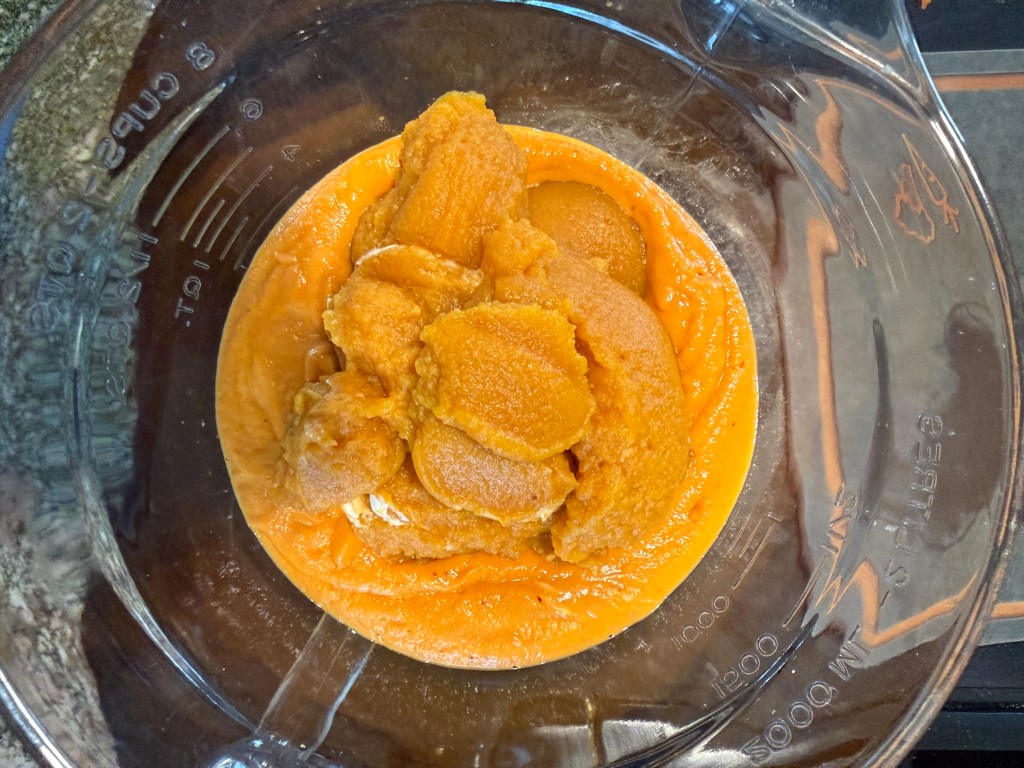 A clear glass bowl containing a mixture of pumpkin puree and whipped cream, showcasing a vibrant orange color.