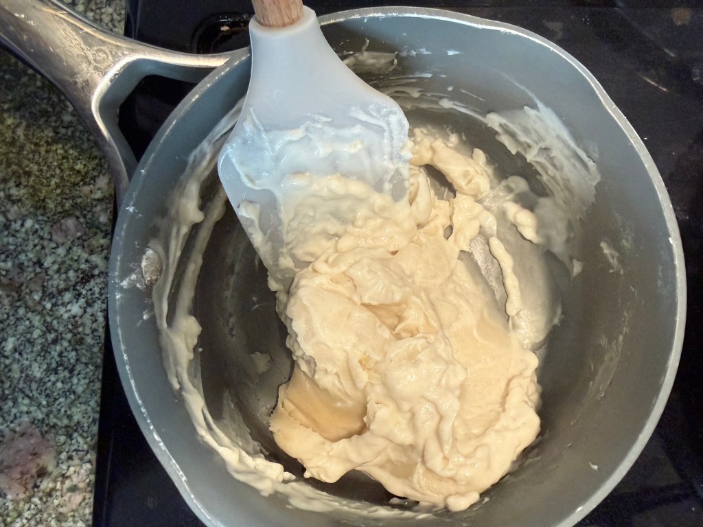 A mixing bowl with thick, beige batter and a spatula, resting on a stovetop.