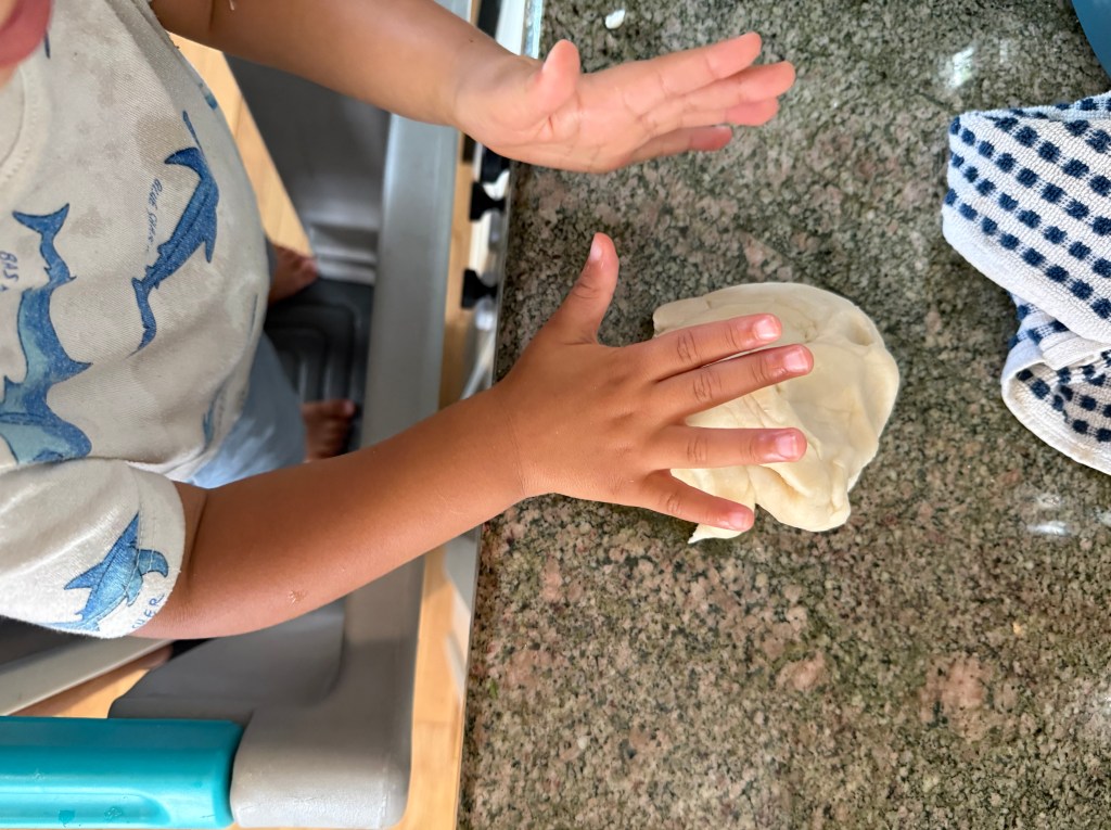 A child playing with dough on a granite countertop, rolling it with their hands.