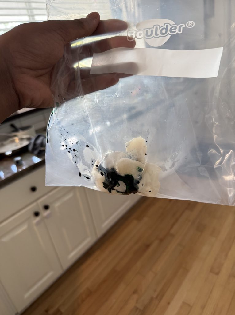 A person holding a clear plastic bag containing a white substance mixed with black and green ink-like liquid.